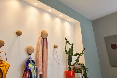 White wall with round wooden coat hooks and warm white LED recessed spotlights for hallway lighting