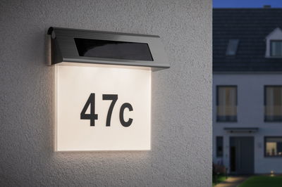 Illuminated house number 47c with solar-powered stainless steel light fixture on white wall