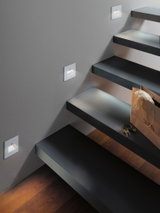 Moderne weiße LED-Treppenwandleuchten mit Bewegungssensor an grauer Wand neben schwarzen Stufen