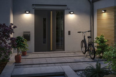 Moderne udendørsbelysning med sorte væglamper ved indgang med grå dør og cykel.