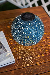 Round blue metal solar lantern with pattern casting decorative light spots on wooden table.