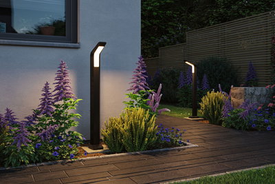 Moderne zwarte metalen LED-buitenlampen verlichten tuinpad met kleurrijke bloemen en houten schutting
