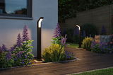 Modern black metal LED outdoor lights illuminate garden path with colorful flowers and wooden privacy fence