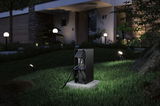 Black outdoor metal power outlet on concrete base in garden with LED landscape lighting at night
