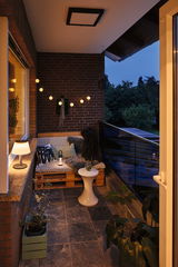 Balcon confortable avec banc en palette bois, coussins blancs et guirlande LED blanc chaud pour éclairage d'ambiance.