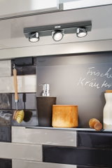 Modern black three-light LED ceiling lamp with dimmable spots above kitchen shelf.