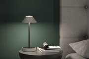 Moderne graue Tischlampe aus Metall mit Stoffschirm auf Nachttisch neben grauem Polsterbett
