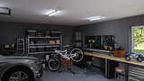 Moderne Garage mit grauem Auto, Fahrrad auf Reparaturständer und gut organisierter Werkbank mit LED-Deckenleuchten