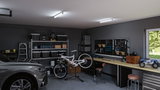 Moderne garage met grijze auto, fiets op reparatiestandaard, georganiseerde werkbank en heldere LED-plafondlampen