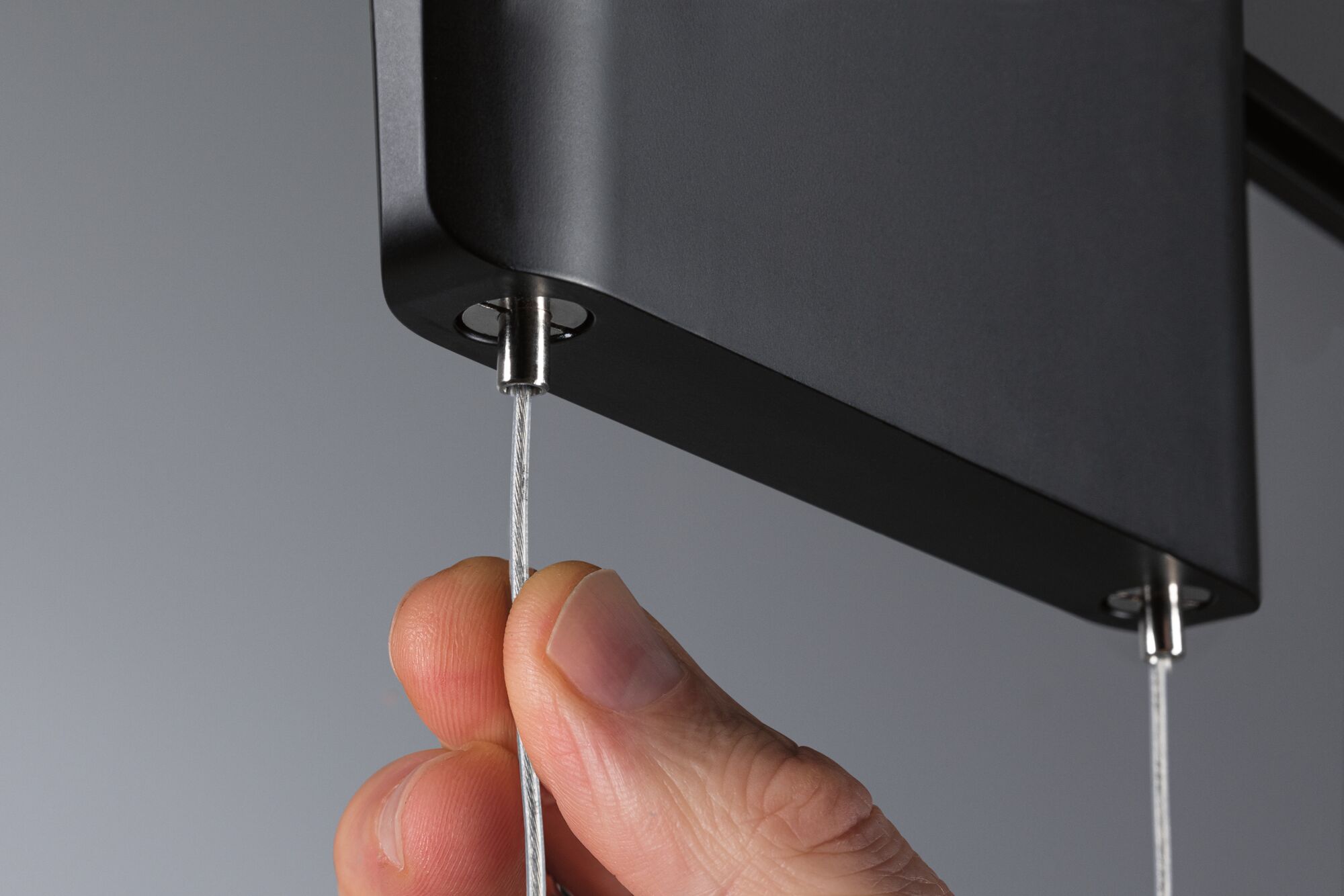 Hand justiert dünnes Stahlseil an schwarzem Aluminium-Pendelleuchtengehäuse für moderne Beleuchtung.