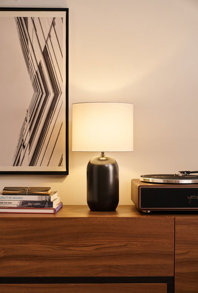 Modern table lamp with black metal base and white fabric shade on wooden sideboard next to turntable.
