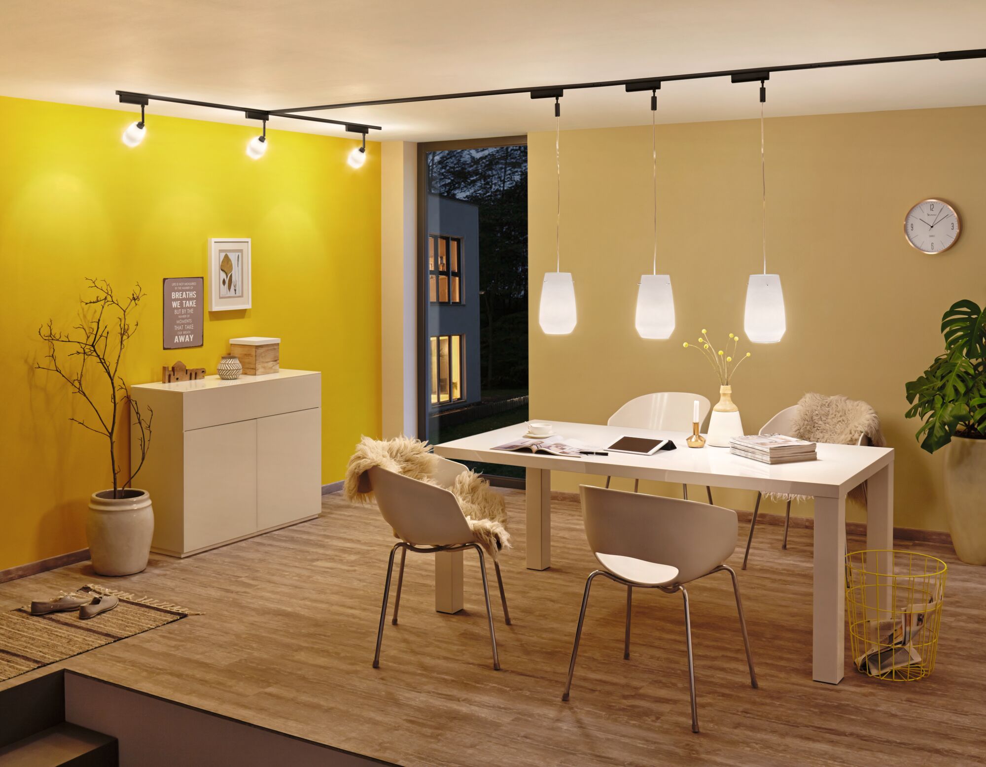 Moderne eetkamer met witte stoelen, houten vloer en drie witte hanglampen aan zwarte rails