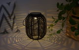 Black rattan lantern with warm light casting decorative shadows for cozy ambiance lighting.