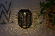 Sort rattanlanterne med varmt lys, der kaster dekorative skygger til hyggelig belysning.