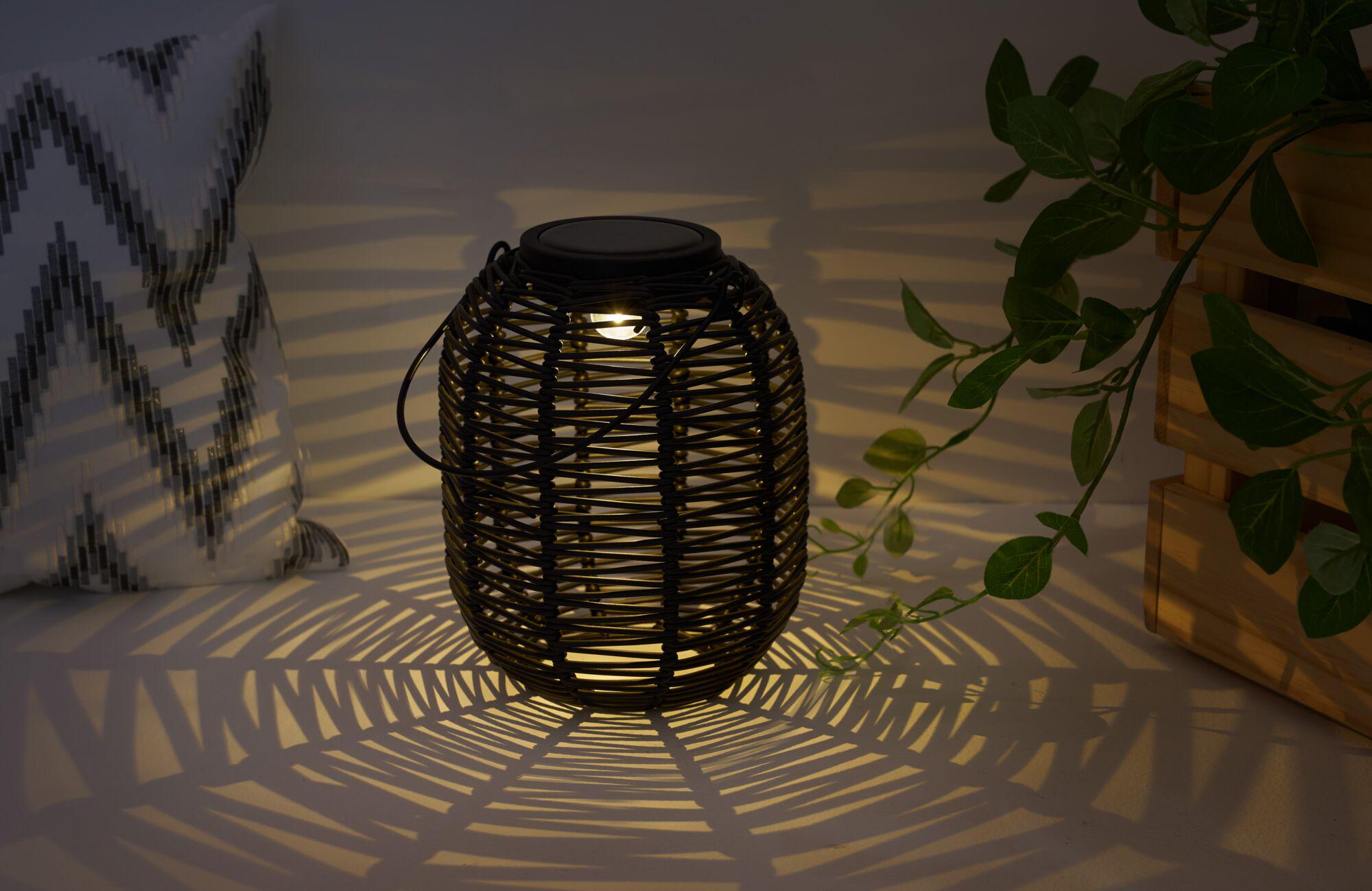 Sort rattanlanterne med varmt lys, der kaster dekorative skygger til hyggelig belysning.