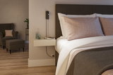 Modern bedroom with brown fabric bed, beige wall lamp and floating wooden bedside table