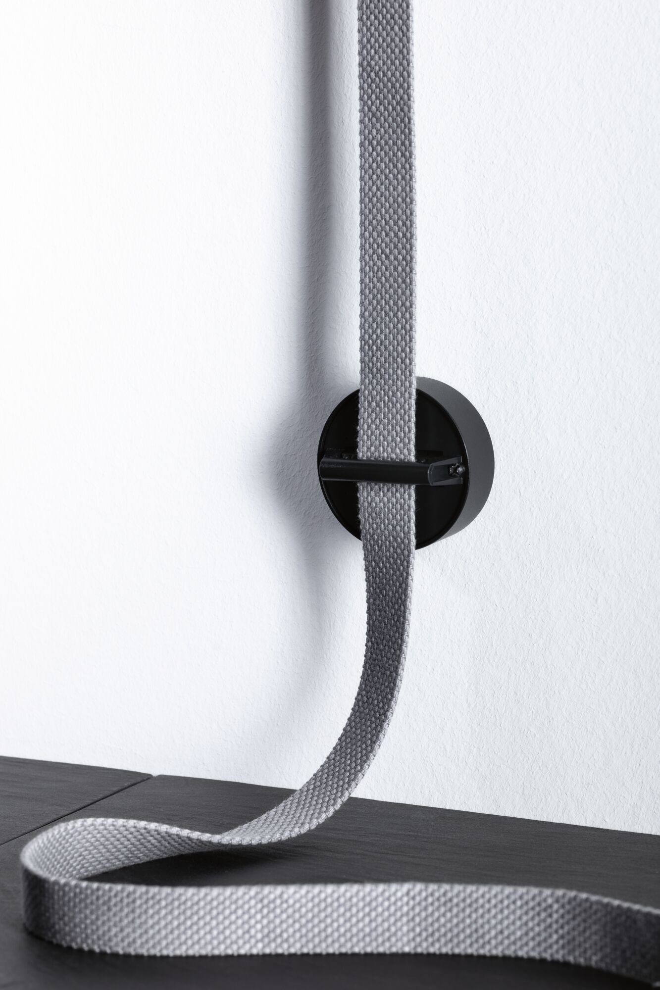 Black wall mount with grey textile strap on white wall for cable management and organization