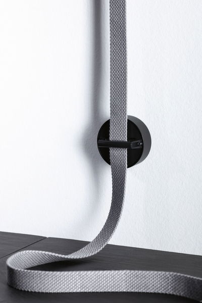 Support mural noir avec sangle textile grise sur mur blanc pour gestion et organisation des câbles