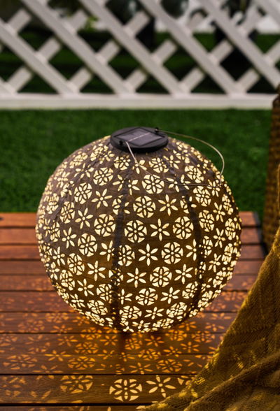 Ronde bruine metalen solar-lantaarn met bloemmotieven die decoratieve lichtpatronen buiten werpt