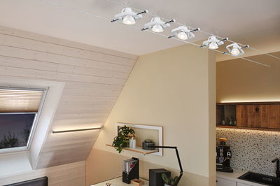 Modern white cable spotlight with five adjustable lamps in bright living space with skylight window.