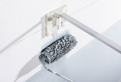 Grijze verfroller met lange steel die een witte muur schildert bij een stopcontact