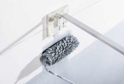 Grauer Farbroller mit langem Stiel beim Streichen einer weißen Wand nahe Steckdose