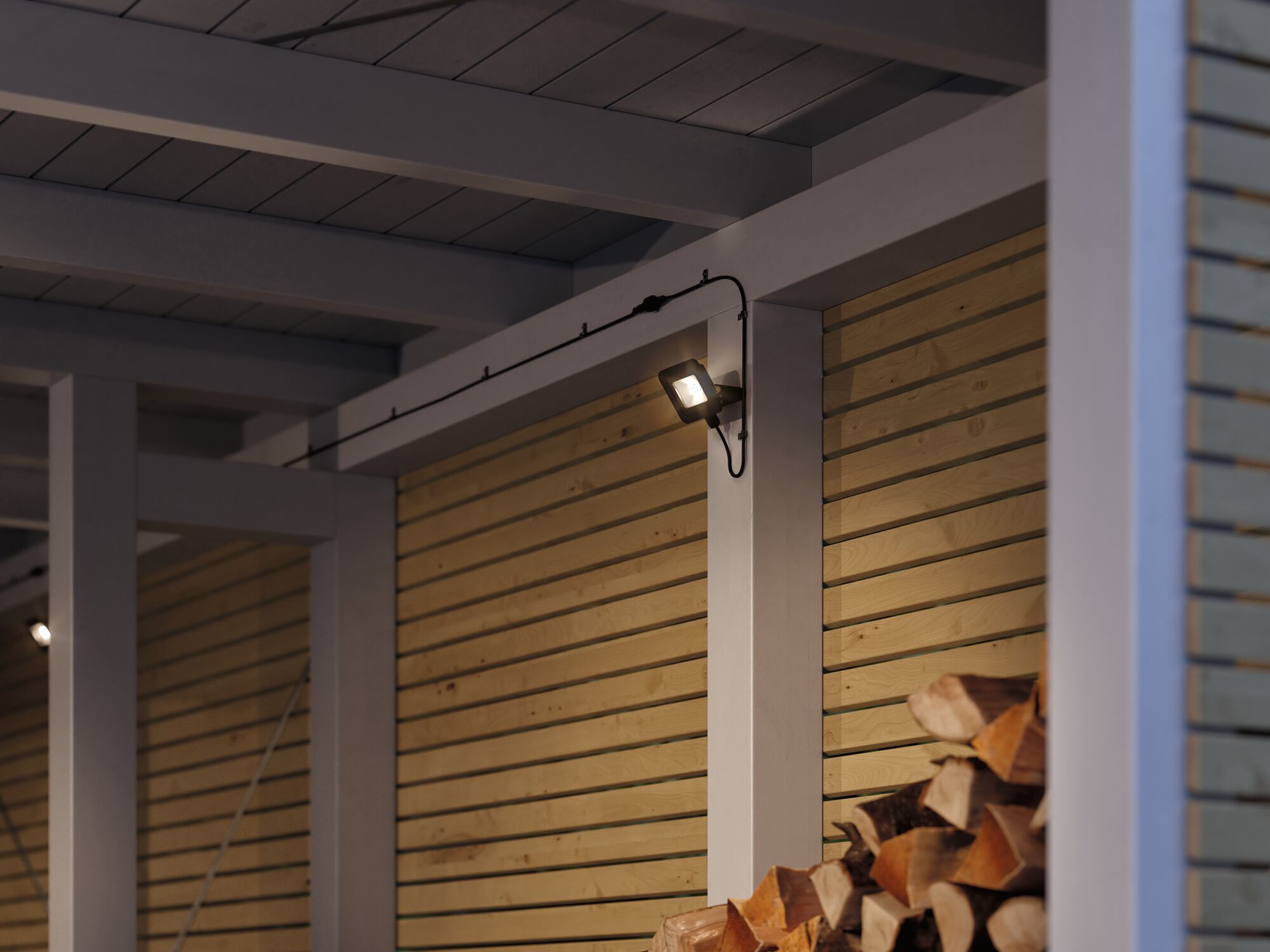 Moderner schwarzer LED-Außenstrahler an weißer Holzwand mit Holzstapel im Vordergrund