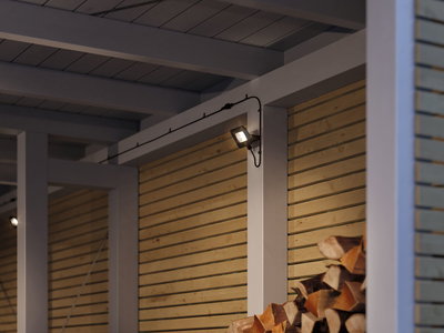 Moderner schwarzer LED-Außenstrahler an weißer Holzwand mit Holzstapel im Vordergrund