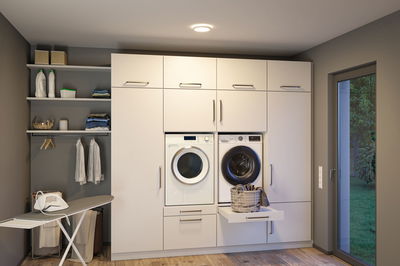 Moderne weiße Einbau-Waschküche mit Waschmaschine, Trockner und integriertem Wäschekorb in Schublade.