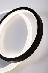 Modern LED wall light with two intertwined black rings emitting warm white light
