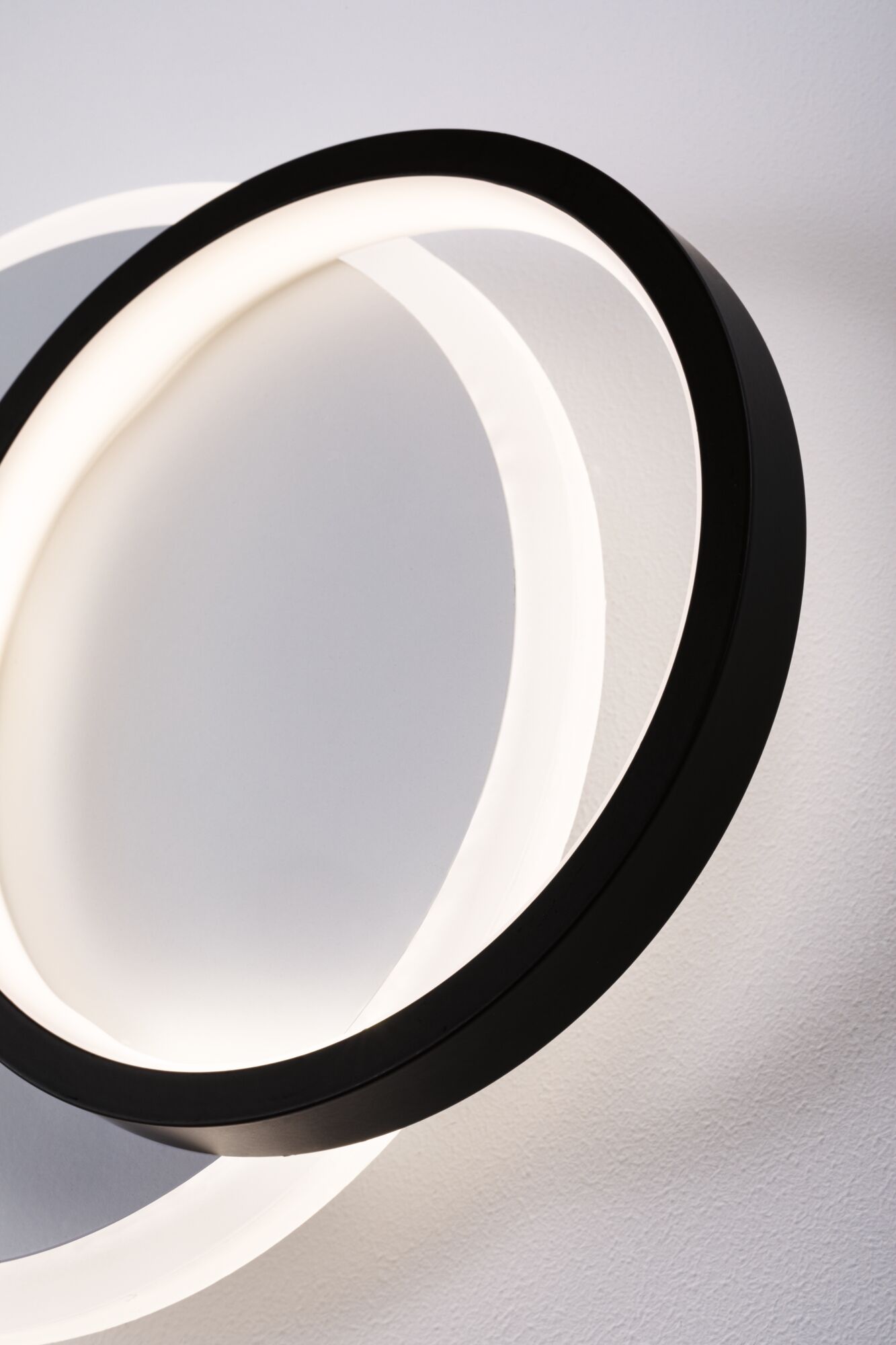 Applique murale LED moderne avec deux anneaux noirs entrelacés diffusant une lumière blanc chaud