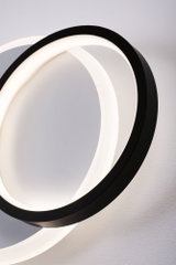 Applique murale LED moderne avec deux anneaux noirs entrelacés diffusant une lumière blanc chaud