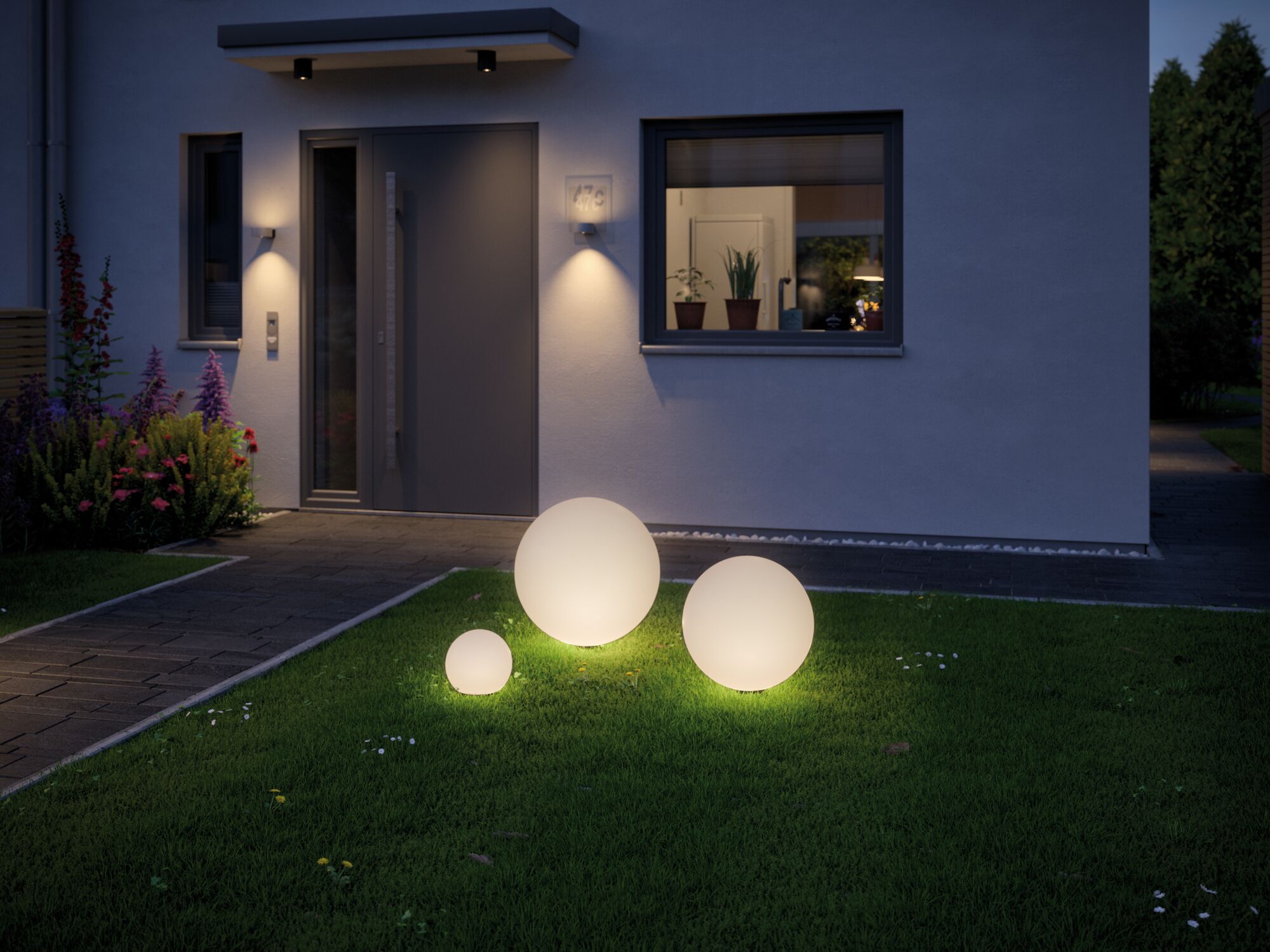Drie witte bolvormige tuinlampen op groen gras voor modern huis met entreeverlichting