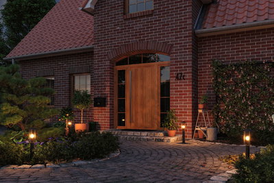 Entree met houten voordeur en warmwitte buitenlampen op zwarte metalen palen langs tuinpad.