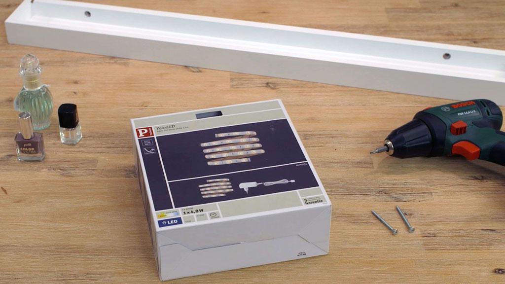 LED-Lichtleisten-Verpackung auf Holztisch mit Bohrmaschine und Nagellackflaschen für DIY-Beleuchtung.