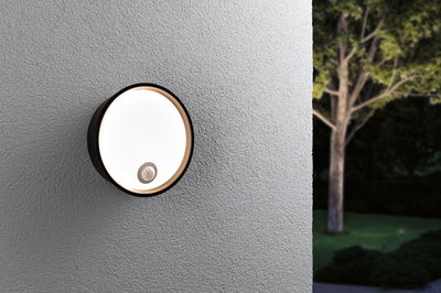 Round black outdoor wall light with motion sensor on grey wall, modern LED garden lighting