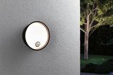 Round black outdoor wall light with motion sensor on grey wall, modern LED garden lighting