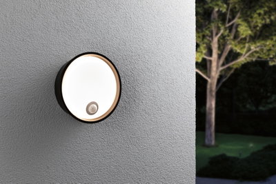 Round black outdoor wall light with motion sensor on grey wall, modern LED garden lighting
