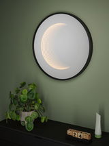 Round LED wall light with black frame and warm white light in modern room with plant and calendar.
