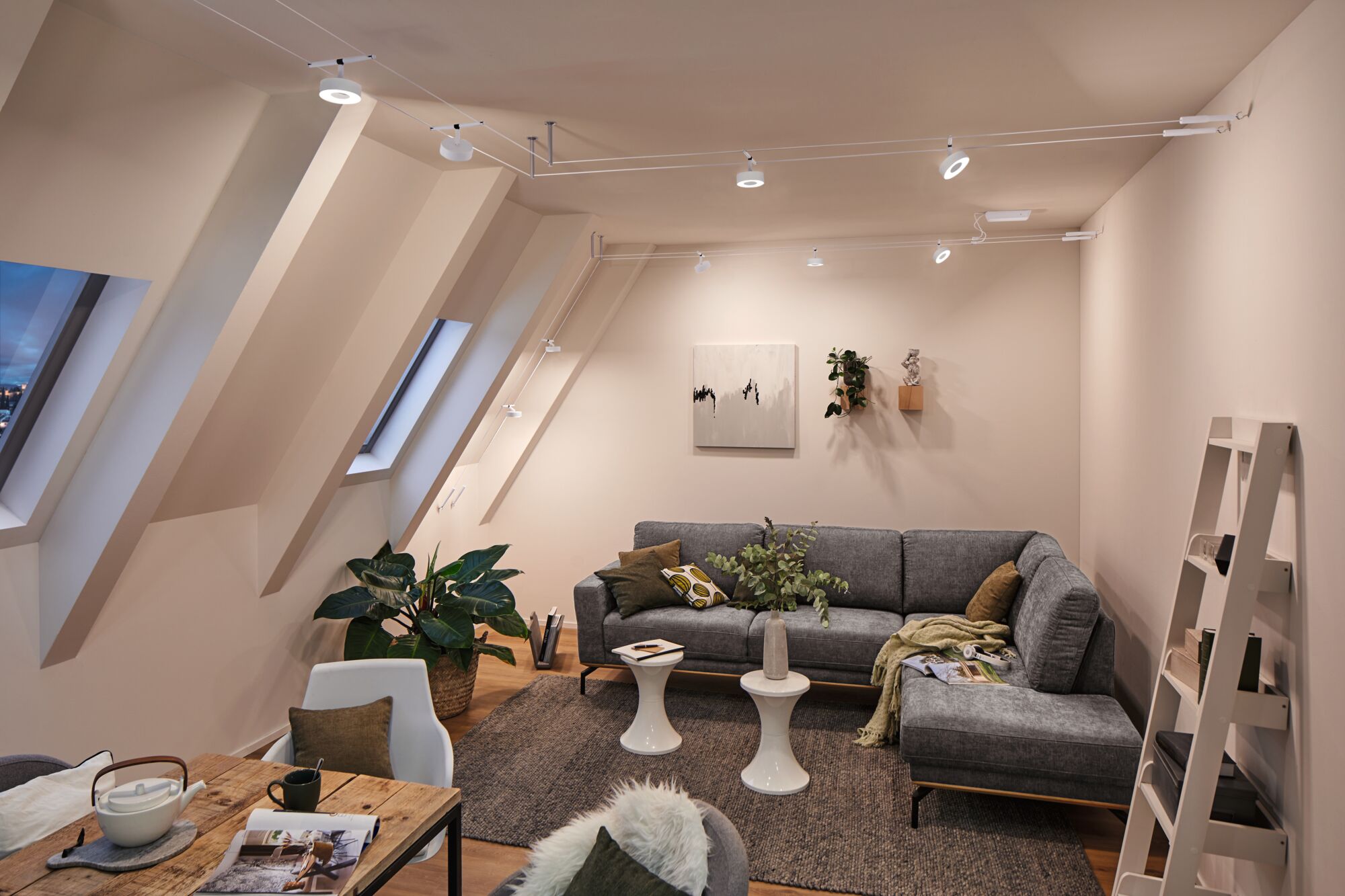 Salon moderne avec canapé en tissu gris, spots LED blancs sur câble et décoration en bois naturel