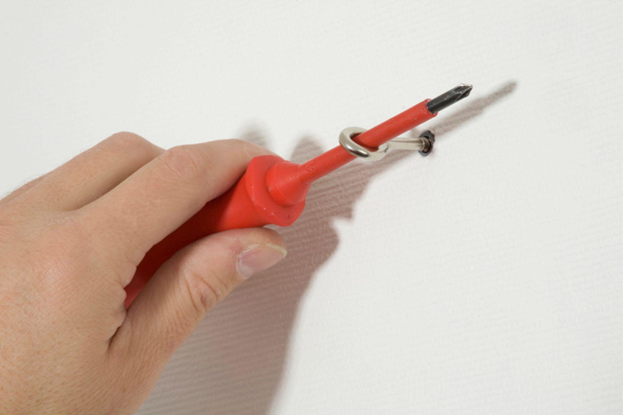 Hånd holder rød skruetrækker, der fastgør metalring på hvid væg til LED-belysning