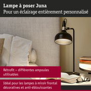Lampe à poser Juna noire en métal avec lumière chaude près d’un canapé et des livres