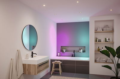 Moderne badkamer met houten wastafel, ronde spiegel en bad met kleurrijke LED-verlichting
