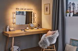 Houten kaptafel met verlichte spiegel en grijs gordijn in gezellige slaapkamer met decoratie