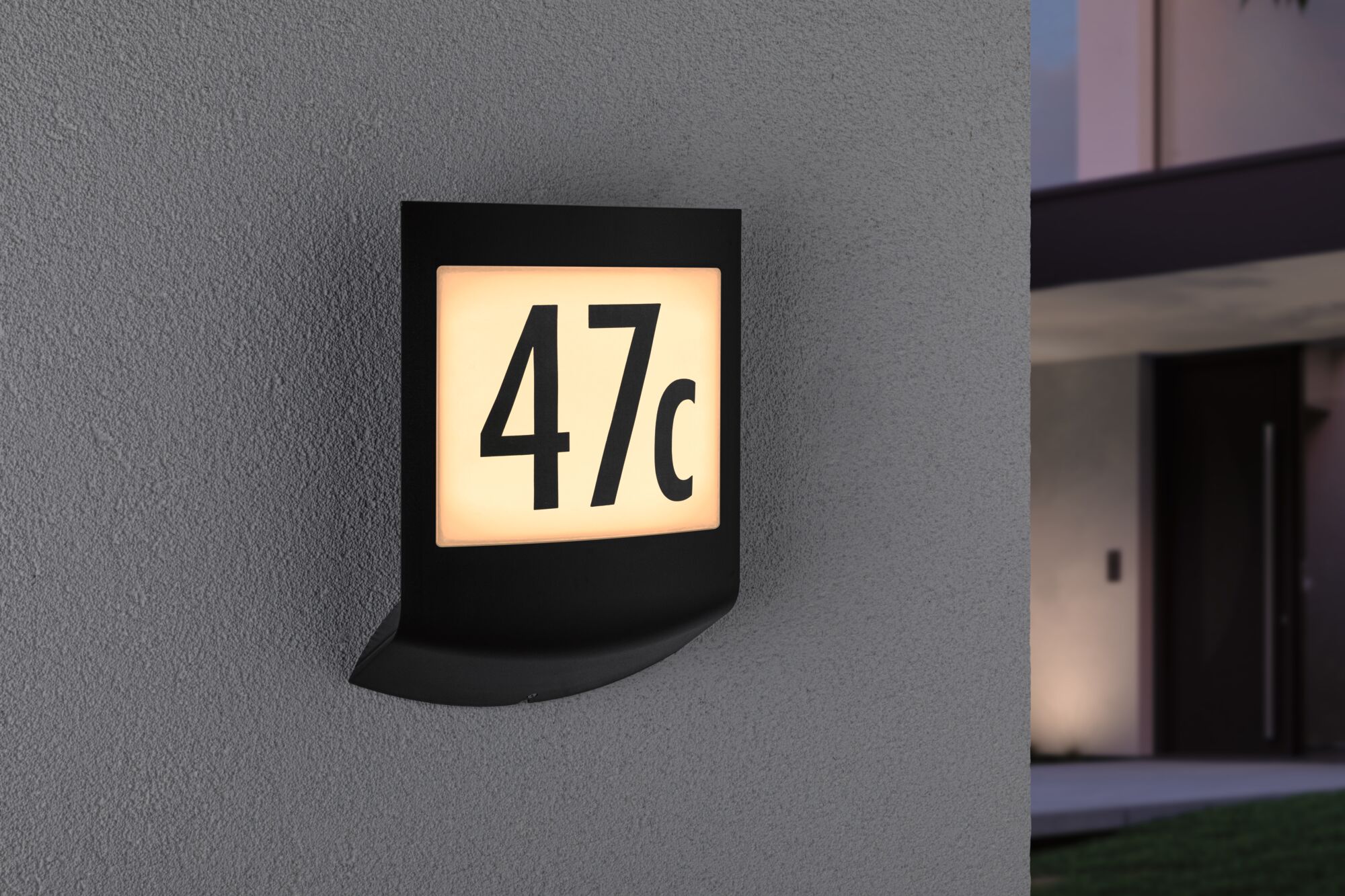 Schwarze LED-Hausnummernleuchte mit beleuchteter Zahl 47c an grauer Außenwand für Hausbeleuchtung