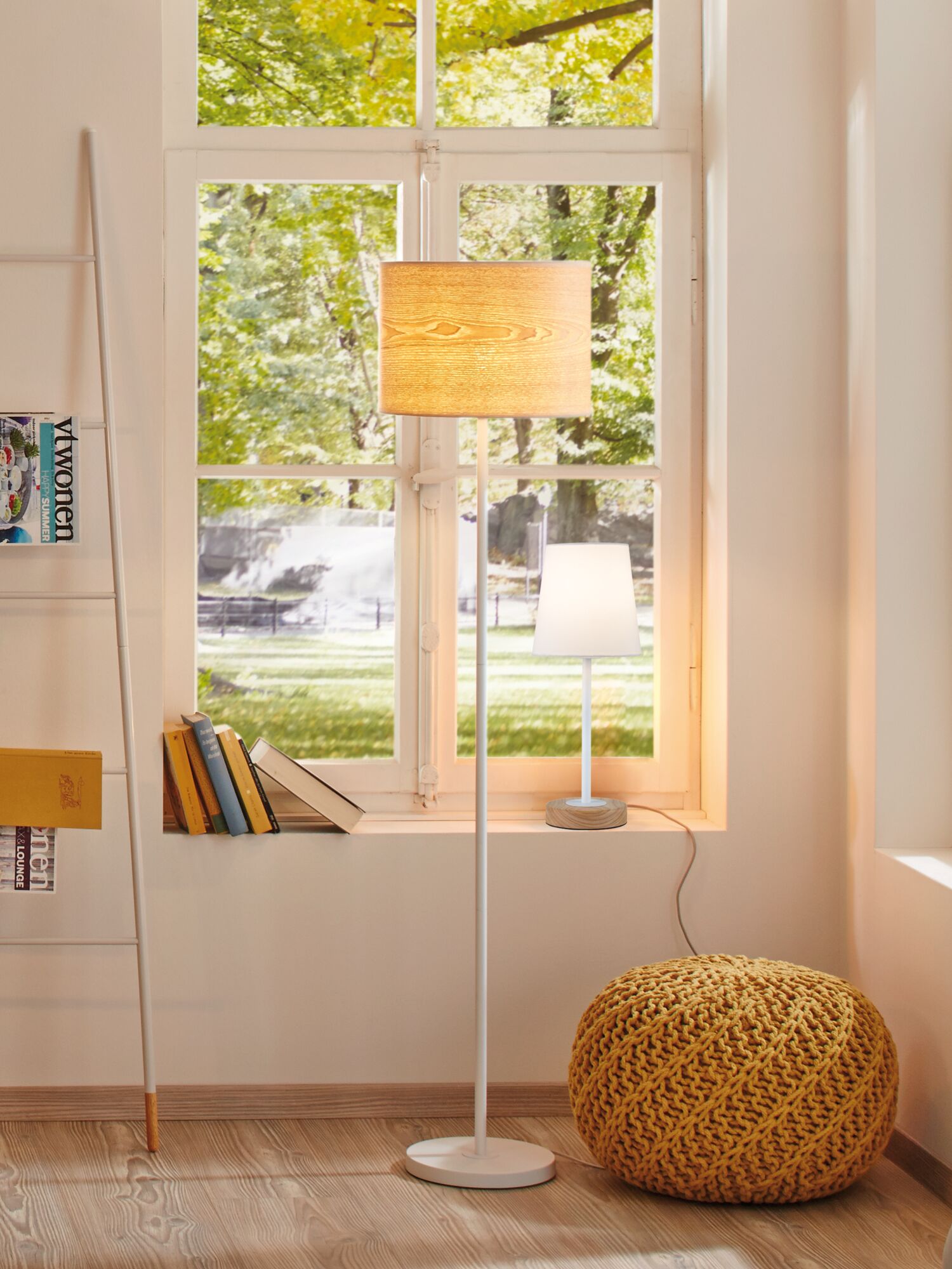 Living room with white floor lamp and wooden base table lamp by window, yellow knitted pouf