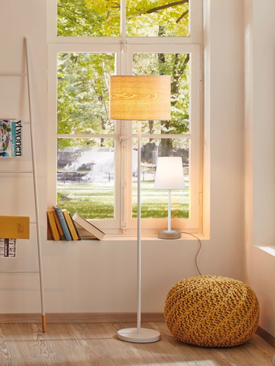 Wohnzimmer mit weißem Stehlampe und Tischlampe mit Holzfuß vor Fenster, gelber Strickpouf