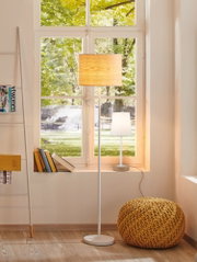 Wohnzimmer mit weißem Stehlampe und Tischlampe mit Holzfuß vor Fenster, gelber Strickpouf