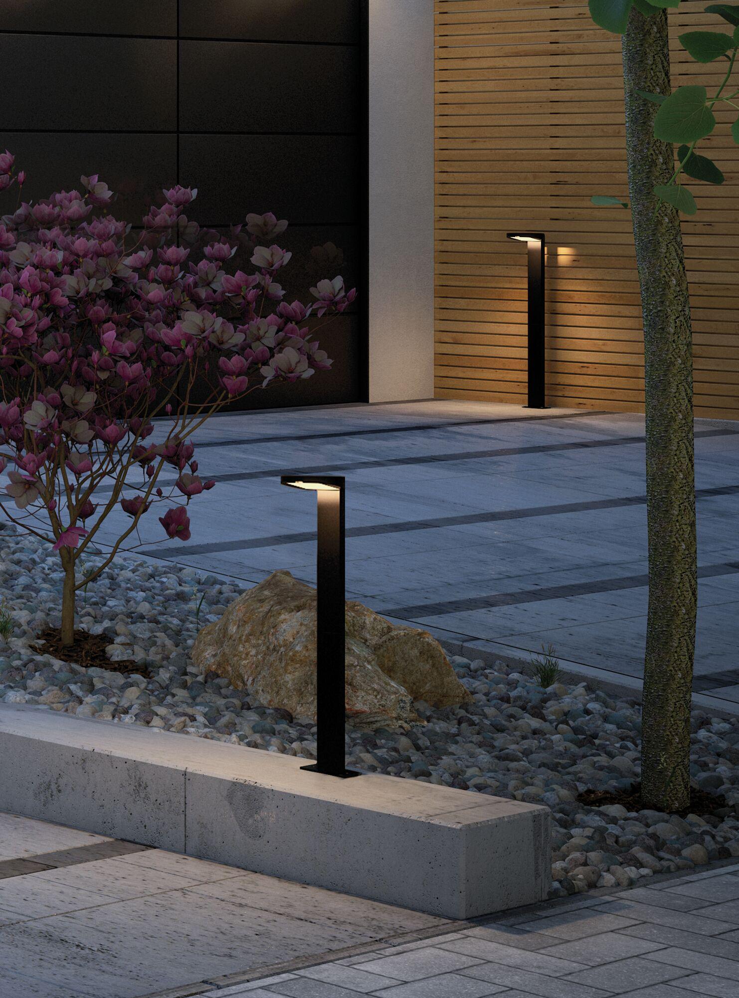 Black modern metal LED pathway light with warm white illumination outdoors by stone pavement.