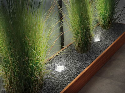 Recessed stainless steel LED floor lights illuminate gravel bed with green grasses, modern energy-saving lighting